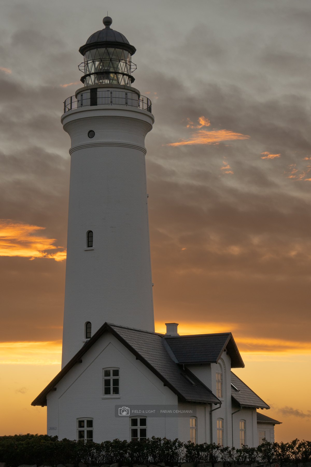 Hirtshals Lighthouse rising white above its keeper’s house against burning evening clouds