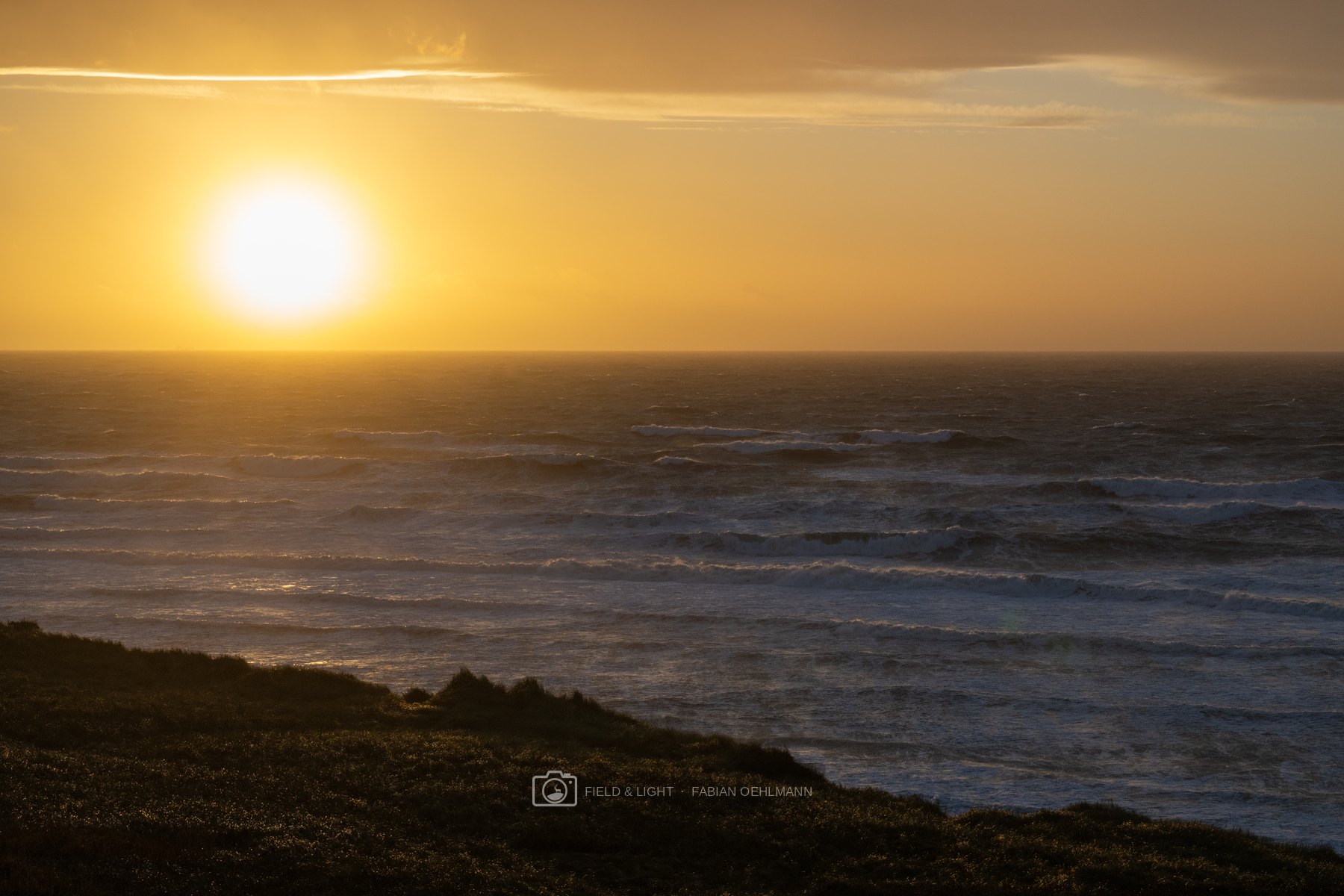 The low evening sun burning gold above rows of wind-driven surf on the North Sea