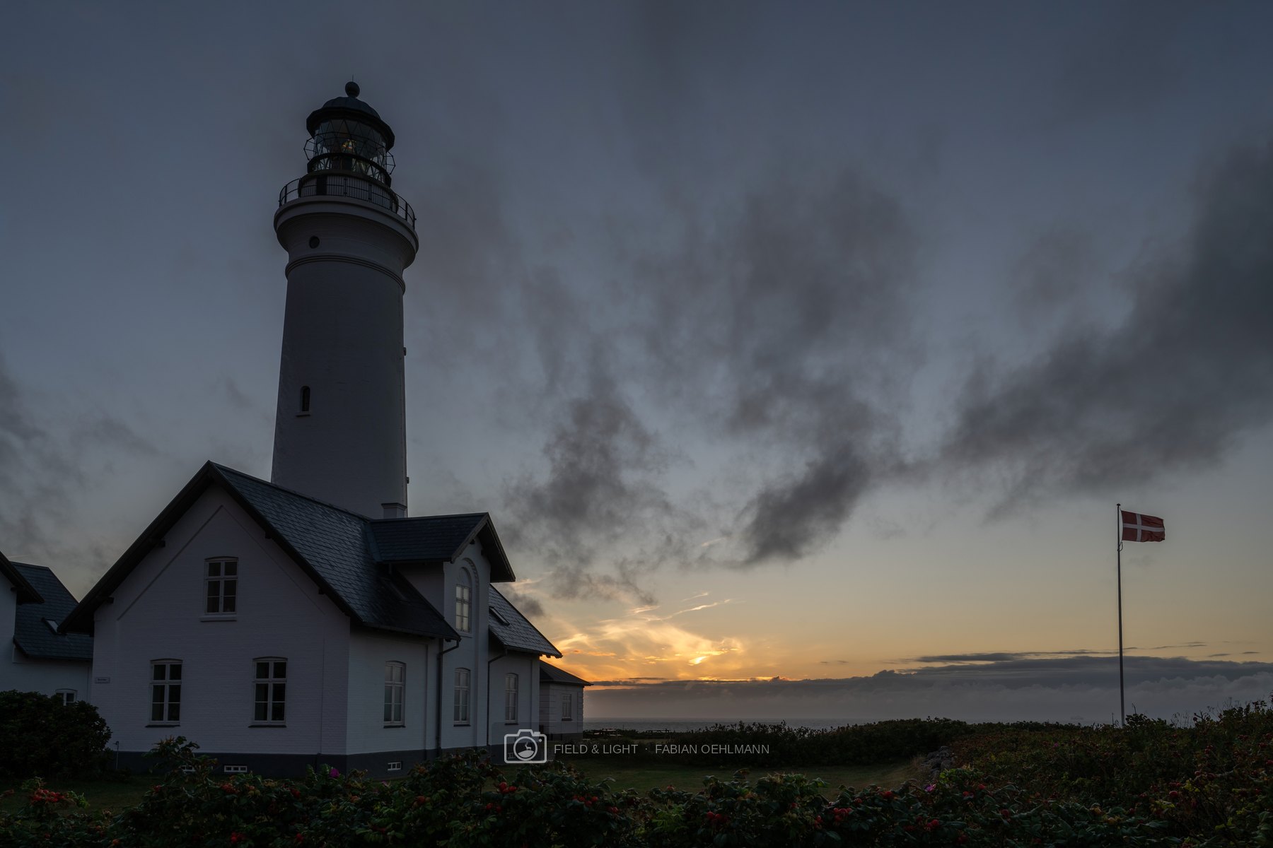 Hirtshals Lighthouse and the Danish flag beneath storm clouds at sunset
