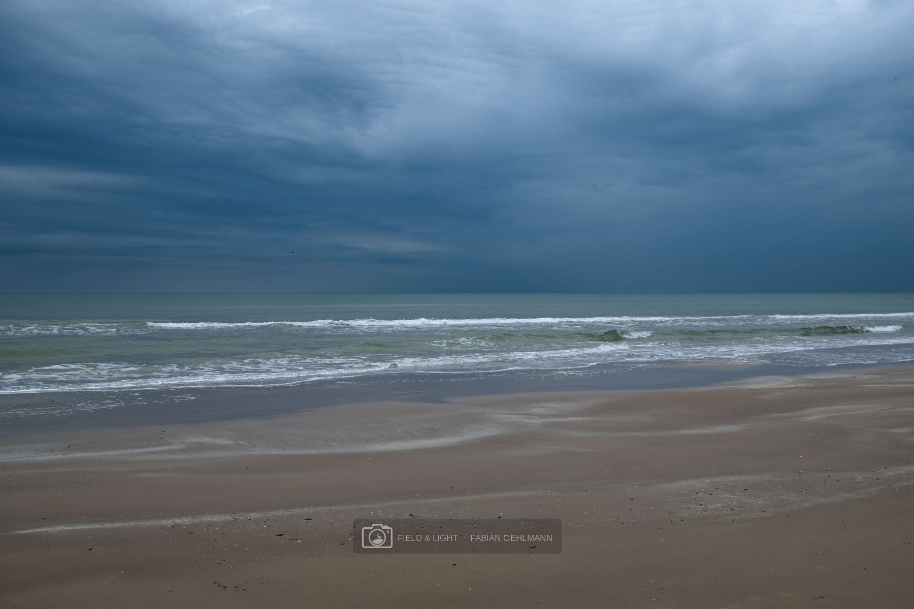 An empty North Sea beach beneath a heavy dark storm sky